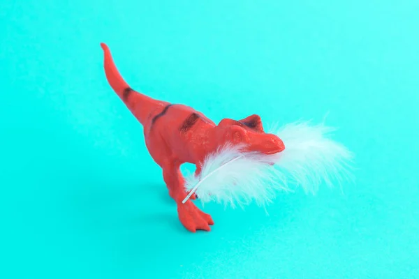 Toy red dinosaur tyrannosaurus rex with soft feather on a turquoise background. Minimalism creative layout