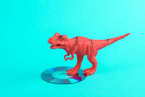 Toy red dinosaur tyrannosaurus rex with cd disk on a turquoise background. Minimalism creative layout