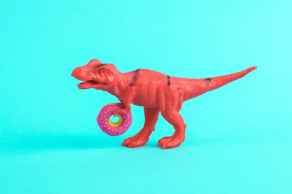 Toy red dinosaur tyrannosaurus rex with donut on a turquoise background. Minimalism creative layout