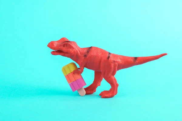 Toy red dinosaur tyrannosaurus rex with ice cream on a turquoise background. Minimalism creative layout