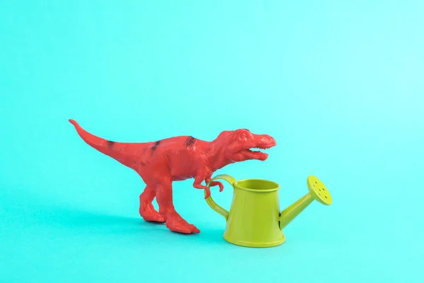 Toy red dinosaur tyrannosaurus rex with watering can on a turquoise background. Minimalism creative layout