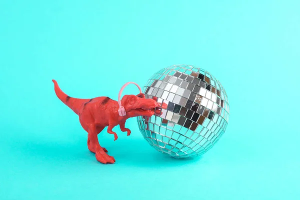 Toy red dinosaur tyrannosaurus rex with disco ball on a turquoise background. Minimalism creative layout