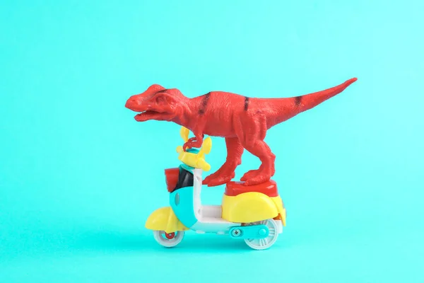 Toy red dinosaur tyrannosaurus rex ride on scooter, turquoise background. Minimalism creative layout.