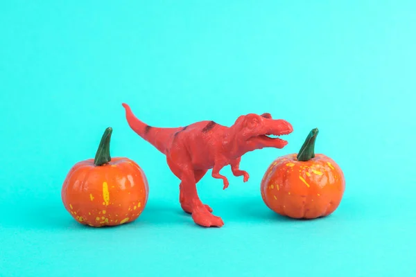 Toy red dinosaur tyrannosaurus rex with halloween pumpkins on a turquoise background. Minimalism creative layout. Trick or treat