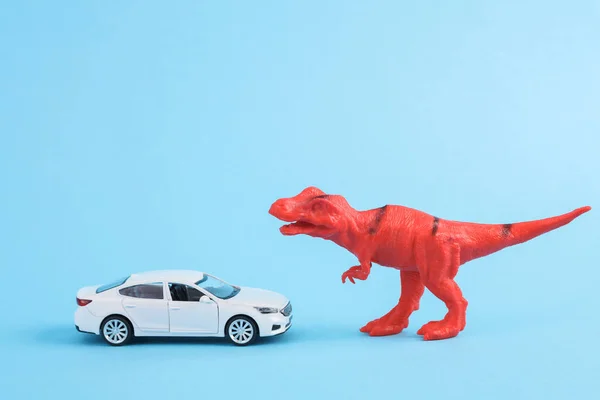 Toy red dinosaur tyrannosaurus rex with car  on blue background. Minimalism creative layout