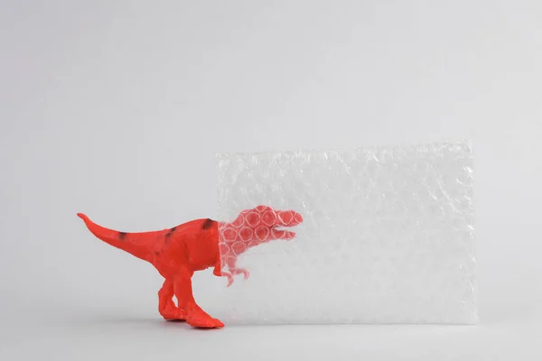 Toy red dinosaur tyrannosaurus rex with bubble wrap on gray background. Minimalism creative layout