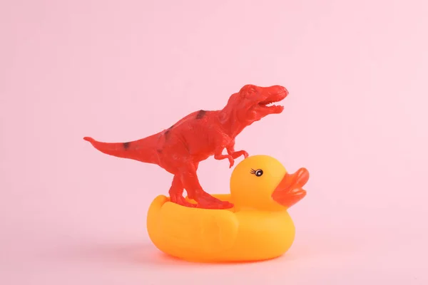 玩具红色恐龙霸王龙雷克斯与橡胶鸭粉红背景 简约主义创意布局 — 图库照片