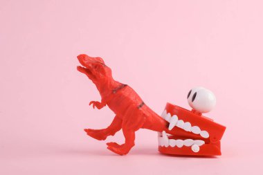 Oyuncak dinozor tyrannosaurus rex pembe arka planda zıplayan çenesiyle. Minimalizmin yaratıcı düzeni