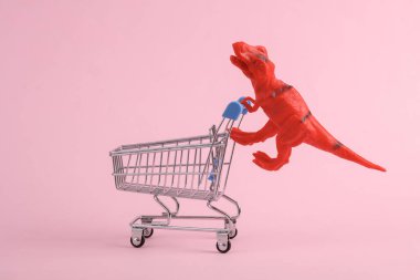 Oyuncak kırmızı dinozor tyrannosaurus rex ve pembe arka planda süpermarket tramvayı. Minimalizmin yaratıcı düzeni