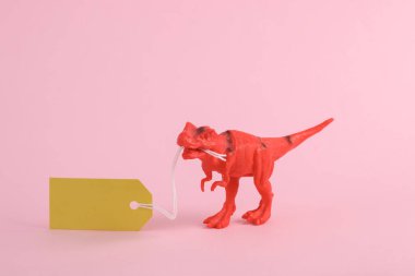 Oyuncak kırmızı dinozor tyrannosaurus rex pembe arka planda fiyat etiketi var. Minimalizmin yaratıcı düzeni