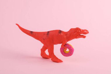 Oyuncak dinozor tyrannosaurus rex pembe arka planda donutla. Minimalizmin yaratıcı düzeni