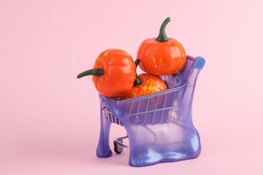Pembe arka planda balkabağı ve balkabağı olan süpermarket arabası. Yaratıcı cadılar bayramı düzeni