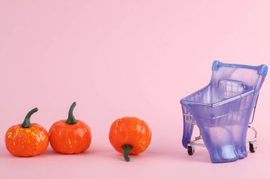 Pembe arka planda balkabağı ve balkabağı olan süpermarket arabası. Yaratıcı cadılar bayramı düzeni