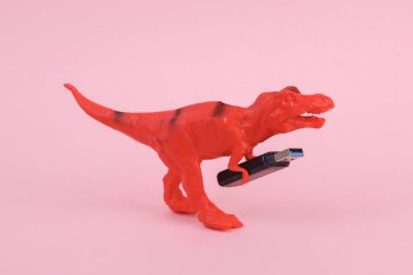 Oyuncak dinozor tyrannosaurus rex pembe arka planda USB et sürücüsüyle. Minimalizmin yaratıcı düzeni