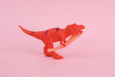 Oyuncak dinozor tyrannosaurus rex pembe arka planda bebek elini tutuyor. Minimalizmin yaratıcı düzeni