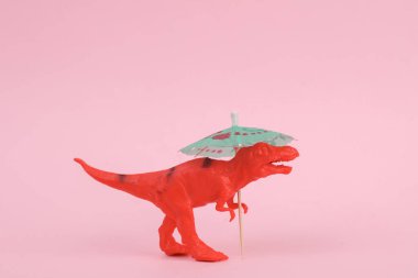 Oyuncak dinozor tyrannosaurus rex pembe arka planda şemsiyesi var. Minimalizmin yaratıcı düzeni