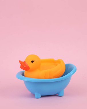 Pembe arka planda oyuncak bir banyoda plastik ördek.