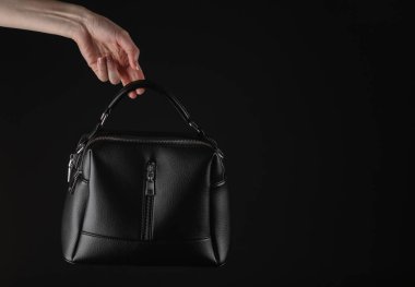 Siyah arka planda siyah deri, lüks bir çanta taşıyan bir kadın.
