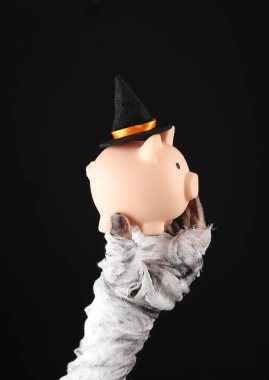 Annenin eli bandaja sarılı ve siyah arka planda izole edilmiş cadı şapkalı domuz kumbarasını tutuyor. Cadılar Bayramı konsepti