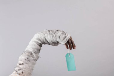 Mumya, gri arka planda boş fiyat etiketini tutuyor. Cadılar Bayramı satış konsepti