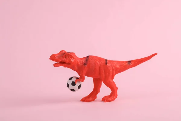 Zabawka Dinozaur Tyranozaur Rex Piłką Nożną Różowym Tle Minimalizm Twórczy — Zdjęcie stockowe