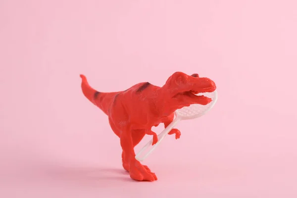 Toy red dinosaur tyrannosaurus rex with tennis racquet on yellow background. Minimalism creative layout