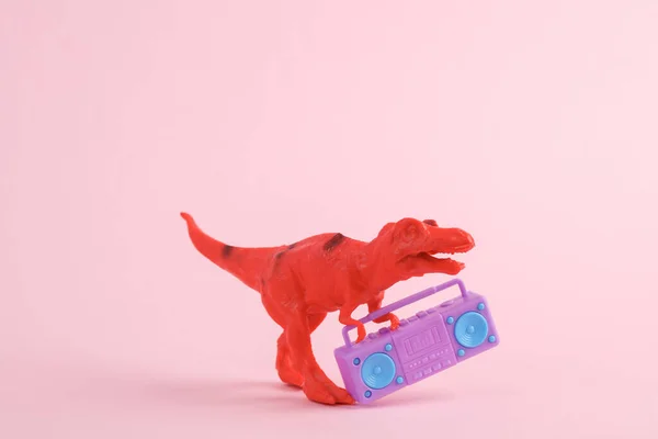 Toy red dinosaur tyrannosaurus rex with boombox audio player on pink background. Minimalism creative layout