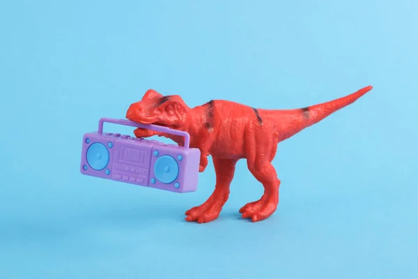 Toy red dinosaur tyrannosaurus rex with boombox audio player on blue background. Minimalism creative layout
