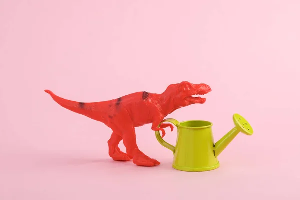 Toy dinosaur tyrannosaurus rex with watering can on pink background. Minimalism creative layout