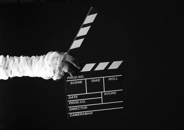 Mummy's hand wrapped in bandage holds movie clapperboard isolated on black background. Halloween, movie concept