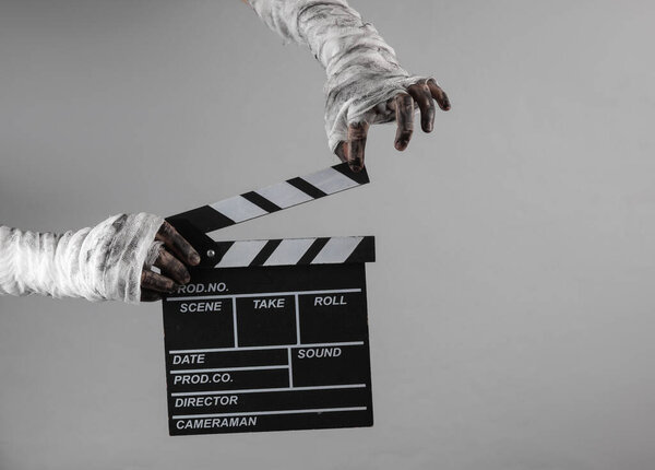Mummy hands wrapped in bandage holds movie clapperboard isolated on gray background. Halloween, movie concept