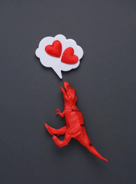 Toy tyrannosaurus rex and Speech bubble with hearts on a gray background