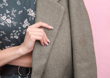 Pembe arka planda poz veren, elbiseli ve yün ceketli moda kadını.