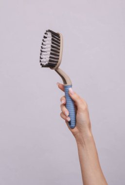 Gri arka planda temizlik fırçası tutan bir kadın.