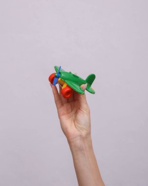 El, gri arka planda oyuncak bir uçağı tutuyor. Seyahat kavramı