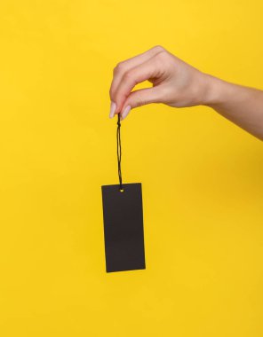 Sarı arka planda siyah bir satış etiketi tutan bir kadın.