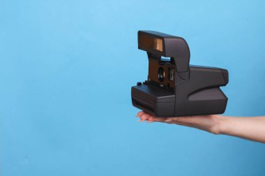 Mavi arka planda bir kadın el kamerasını tutuyor.