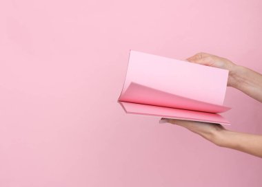 Kadın eli, pembe renkli arka planda pembe kağıtlı bir not defteri tutuyor..