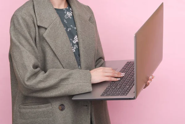 Pembe arka planda dizüstü bilgisayar kullanan yün ceketli bir iş kadını