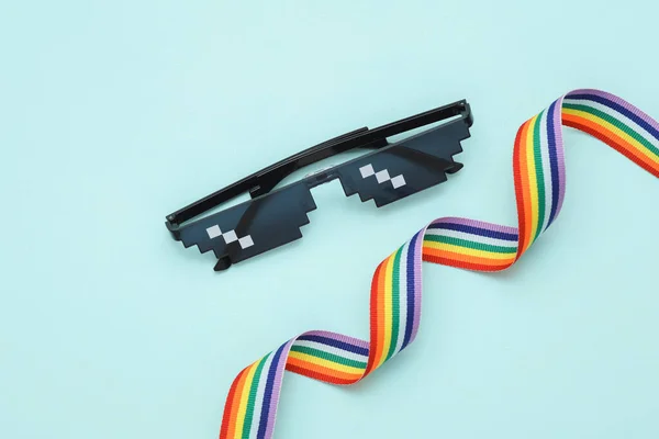 Pixelated 8 bit sunglasses with  lgbt rainbow ribbon on blue pastel background