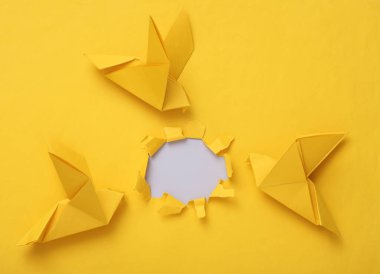 Sarı arkaplanda yırtık delikleri olan sarı origami güvercinleri. Barış sembolü, savaş yok.