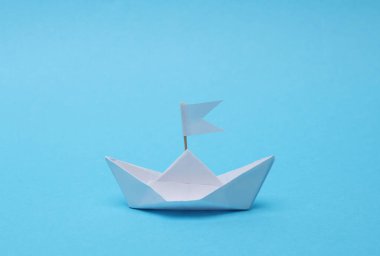 Mavi arka planda bayrağı olan kağıttan bir tekne. Liderlik kavramı