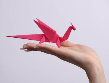 Kadın eli, beyaz arka planda origami Dragon 'u tutuyor. Hobi, yaratıcılık