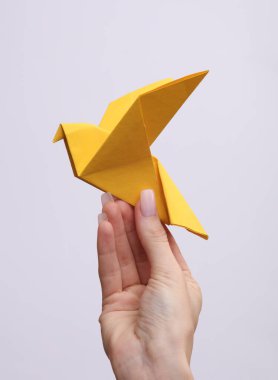 Gri arkaplanda sarı origami kağıt güvercini tutan kadın el.