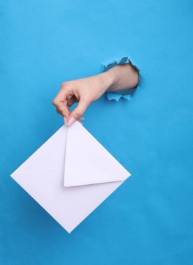 Kadın eli mavi kağıttaki yırtık delikten beyaz bir zarf tutuyor.