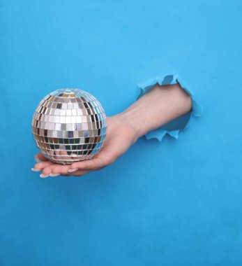 Kadın eli, disko topunu mavi kağıdın yırtık deliğinde tutuyor.