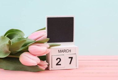 27 Mart tarihli tahta takvimi ve pastel arka planda laleleri engelle. Bahar Kompozisyonu