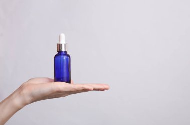 Kadın avucunda serum şişesi, gri arka plan.