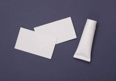 Markalaşma için beyaz boş kartvizitler ve gri arka planda beyaz krema tüpü. Güzellik konsepti. Sunumlar ve kurumsal kimlik için yaratıcı bir model. Üst görünüm