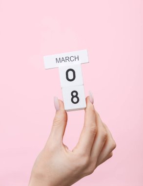 Uluslararası Kadınlar Günü. Ahşap blok takvimi tutan bir kadın. Pembe arka planda tarih 08 Mart.